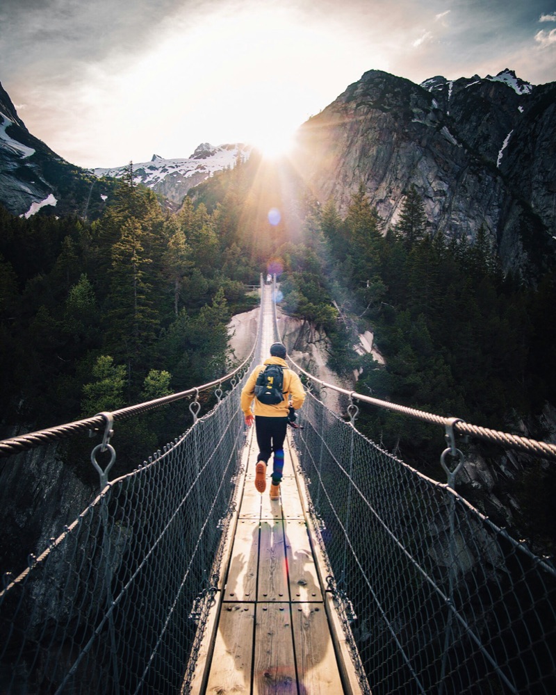 Creator hiking across a suspension bridge in the mountains