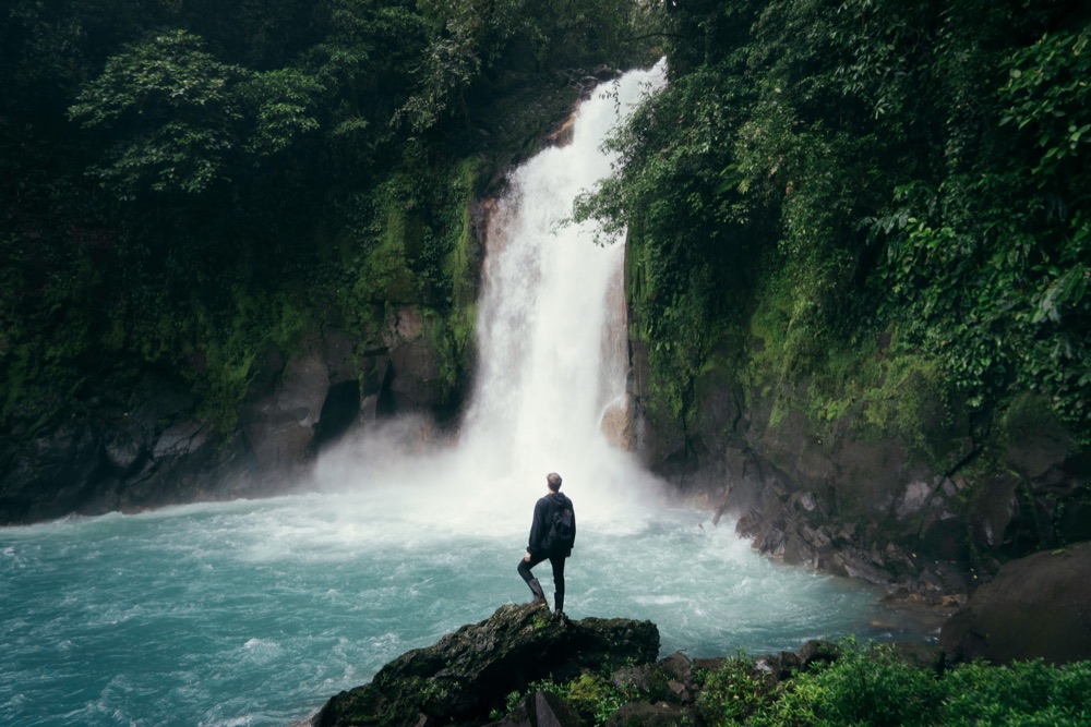 Creator standing before a jungle waterfall